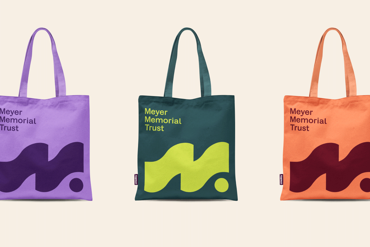 Three colorful Meyer Memorial Trust tote bags in purple, green, and orange, each with a bold wave-and-dot logo