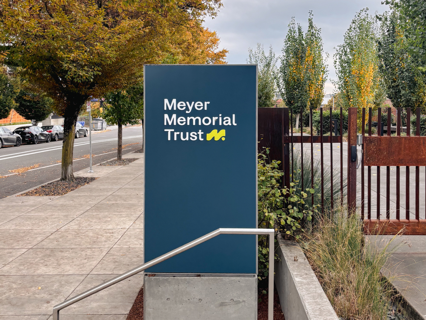 Meyer Memorial Trust Sign with logo next to the sidewalk and trees.