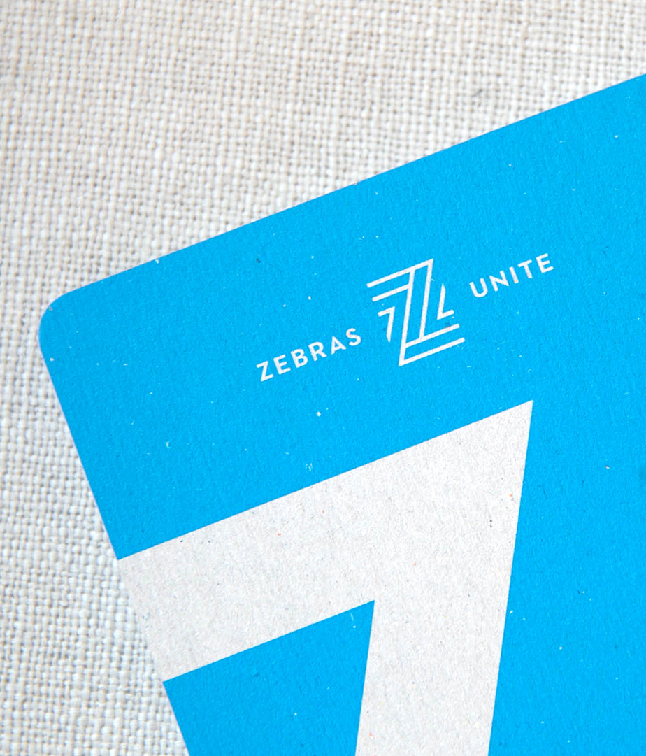 Closeup of the Zebras Unite primary logo on collateral using the brand blue, against a neutral textured background.