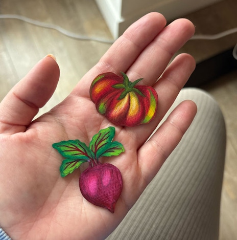 Shrinky dinks in the shape of a tomato and a beet in a person's hand