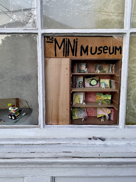 A mini museum nestled into the open space behind a missing pane of a glass window.