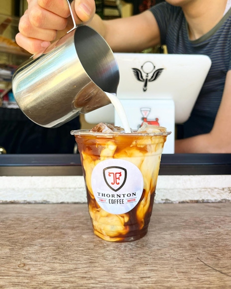 Someone pouring cream into a cup of Thornton coffee.