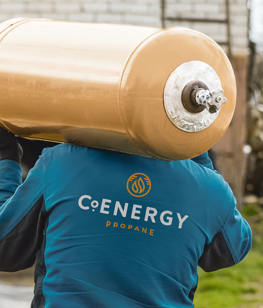 A photograph of a person carrying a propane tank, their back to the camera with the CoEnergy propane logo on the back of their jacket.