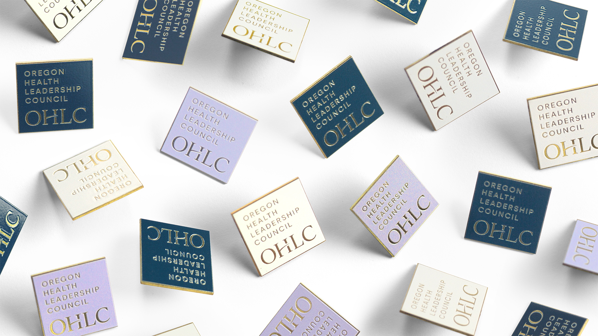 Enamel pins with the Oregon Health Leadership Council logo in a mix of brand colors, on a white background.