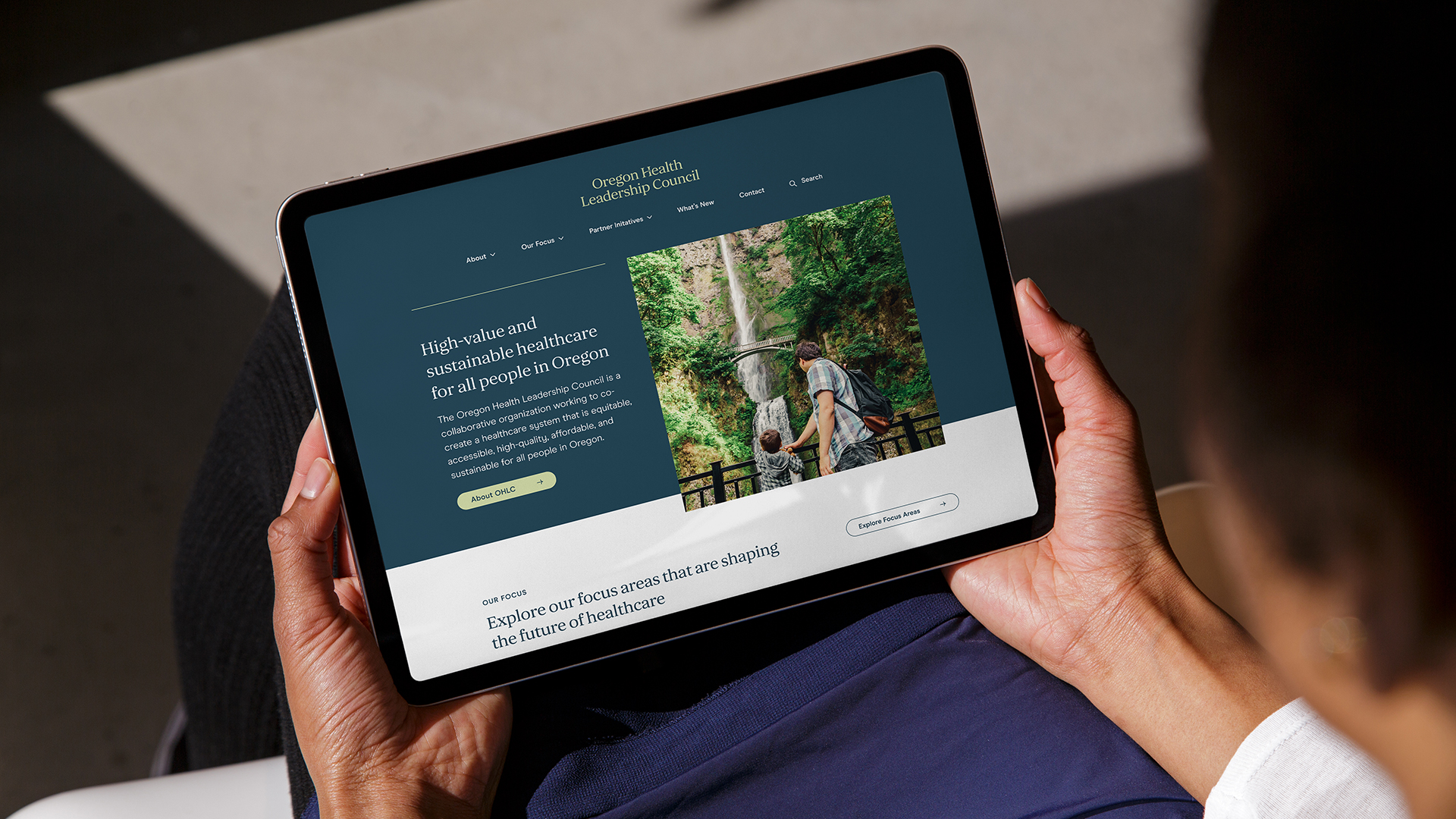 A closely cropped photograph of a tablet in a person's hands, with the OHLC website open in the browser.